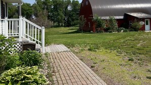A red barn with a metal roof, a white house with a porch, and a paved pathway leading to the house. - Cozy and quaint farmhouse on an acreage  (Mountain Lake)
