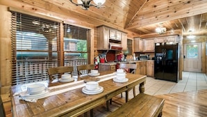Un intérieur en bois avec une table à manger pour quatre personnes, des meubles de rangement en bois et un réfrigérateur noir.
