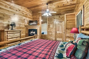 Une chambre à coucher située dans une cabane en rondins, avec un lit, un ventilateur de plafond, une cheminée et une lampe rouge.