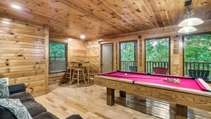 L’intérieur d’un chalet en bois, avec une table de billard, un canapé et une table à manger.