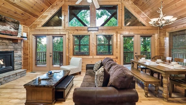 Un intérieur de cabane en bois spacieux, avec un plafond haut, une cheminée, un coin repas et de grandes fenêtres.