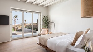Un dormitori amb llit, una cadira, una planta i vista a l'exterior per una porta corredissa.