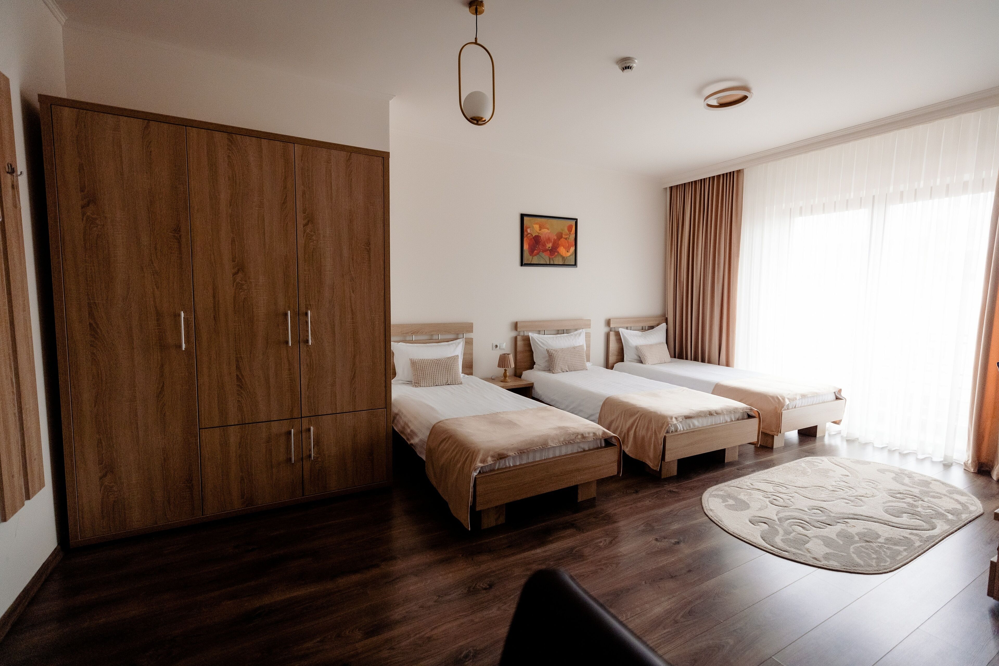A hotel room with two single beds, a wardrobe, a large window with curtains, and a wooden floor.
