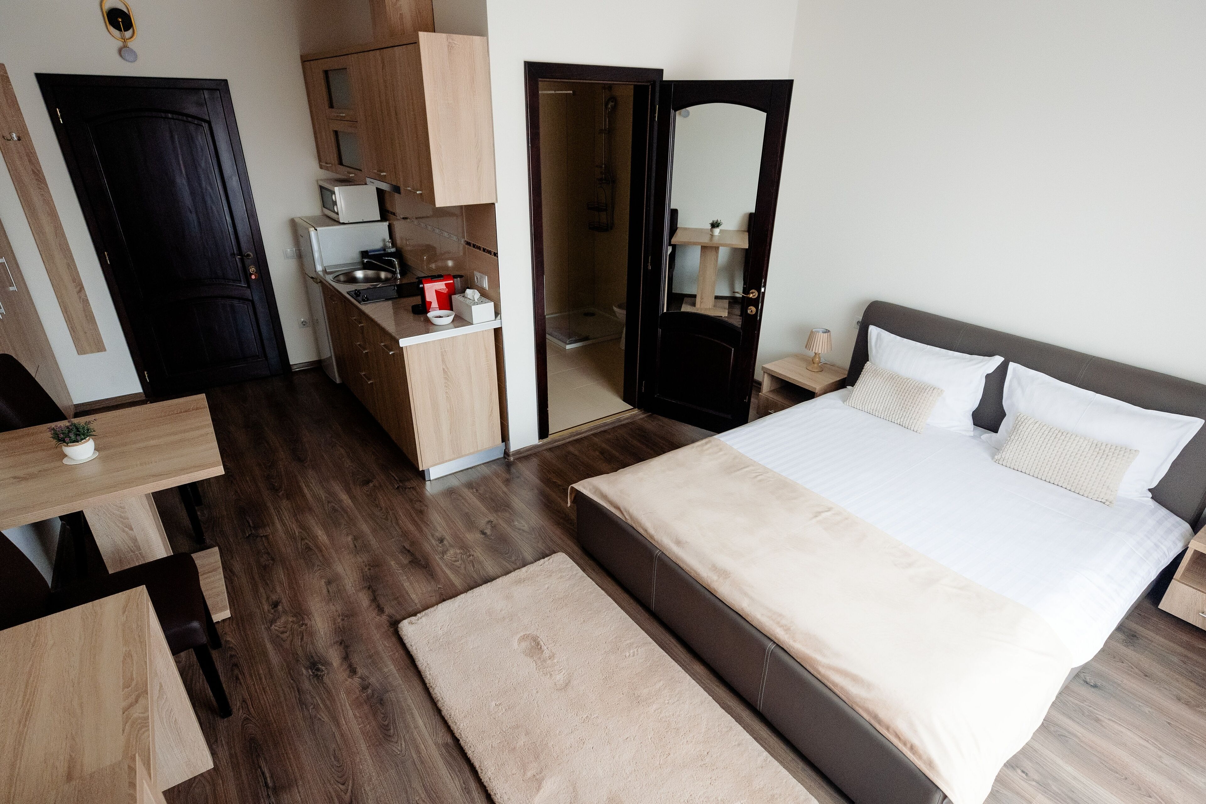 A bedroom with a large bed, a wooden desk, a kitchenette, and a bathroom.