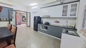 A compact kitchen with modern appliances, a dining area with chairs, and a visible entrance to the outside. - Blue Homestay Cau Giay (Hanoi)
