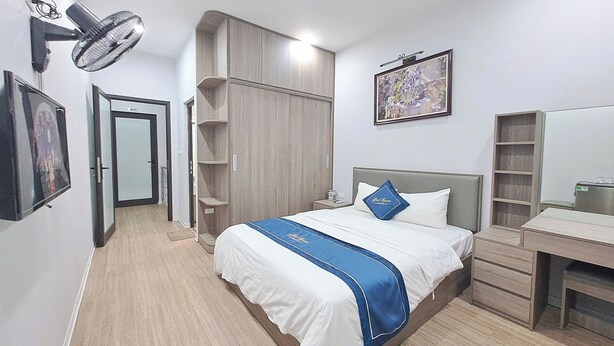 A hotel room with a bed, a desk, a wardrobe, a wall-mounted fan, and a framed picture. - Blue Homestay Cau Giay (Hanoi)