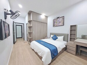 A hotel room with a bed, a desk, a wardrobe, a wall-mounted fan, and a framed picture. - Blue Homestay Cau Giay (Hanoi)