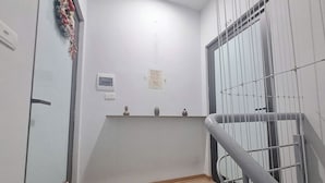 A narrow hallway with a wooden floor, a metal railing, and a door with a decorative wreath. - Blue Homestay Cau Giay (Hanoi)