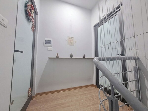 A narrow hallway with a wooden floor, a metal railing, and a door with a decorative wreath. - Blue Homestay Cau Giay (Hanoi)