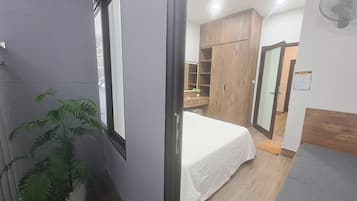 A bedroom with a bed, a wooden wardrobe, a potted plant, and a mirror.