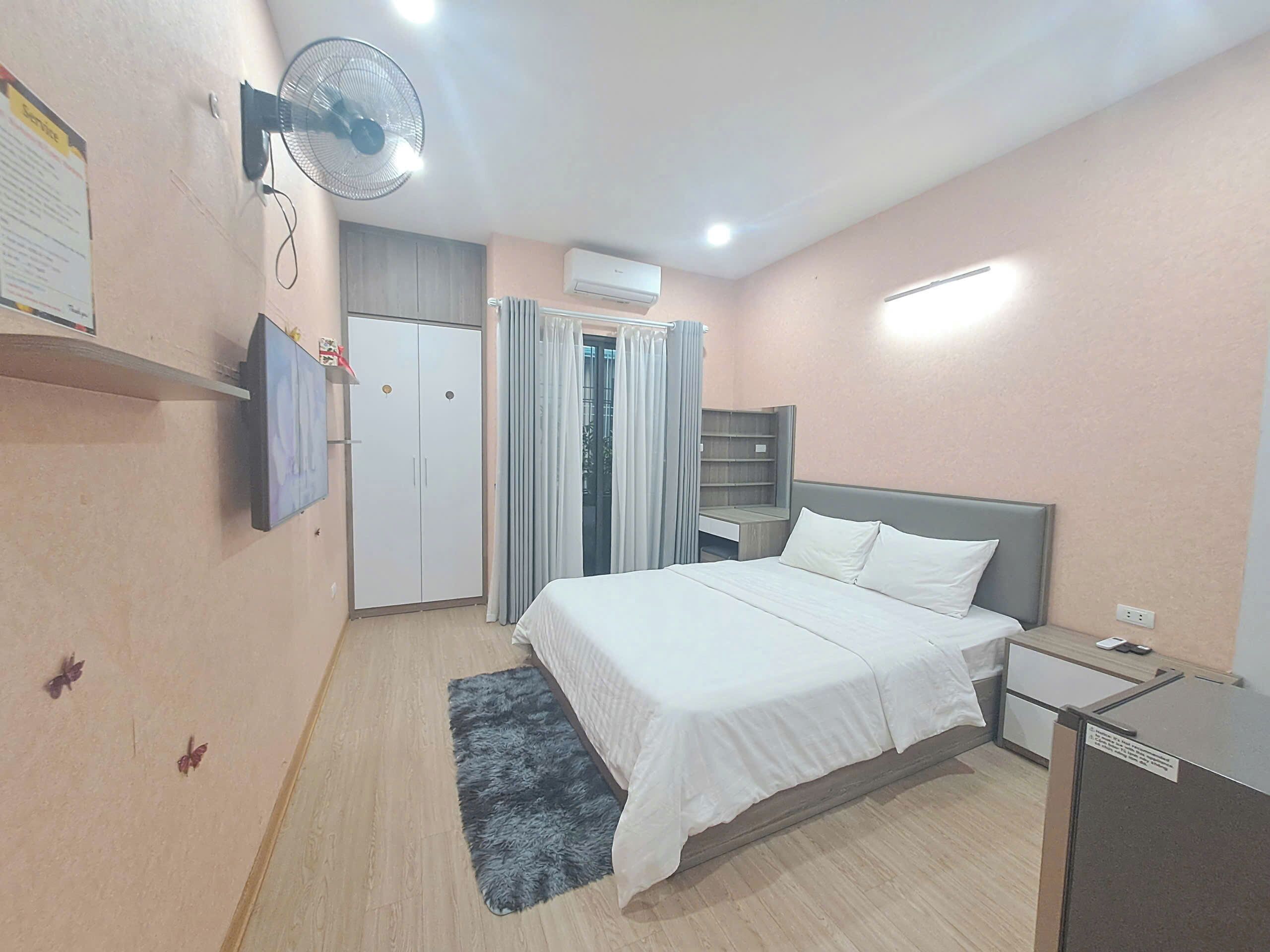 A bedroom with a bed, a wardrobe, a desk, a fan, and an air conditioning unit.