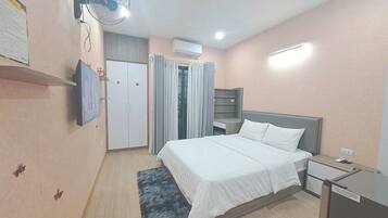 A bedroom with a bed, a wardrobe, a desk, a fan, and an air conditioning unit.