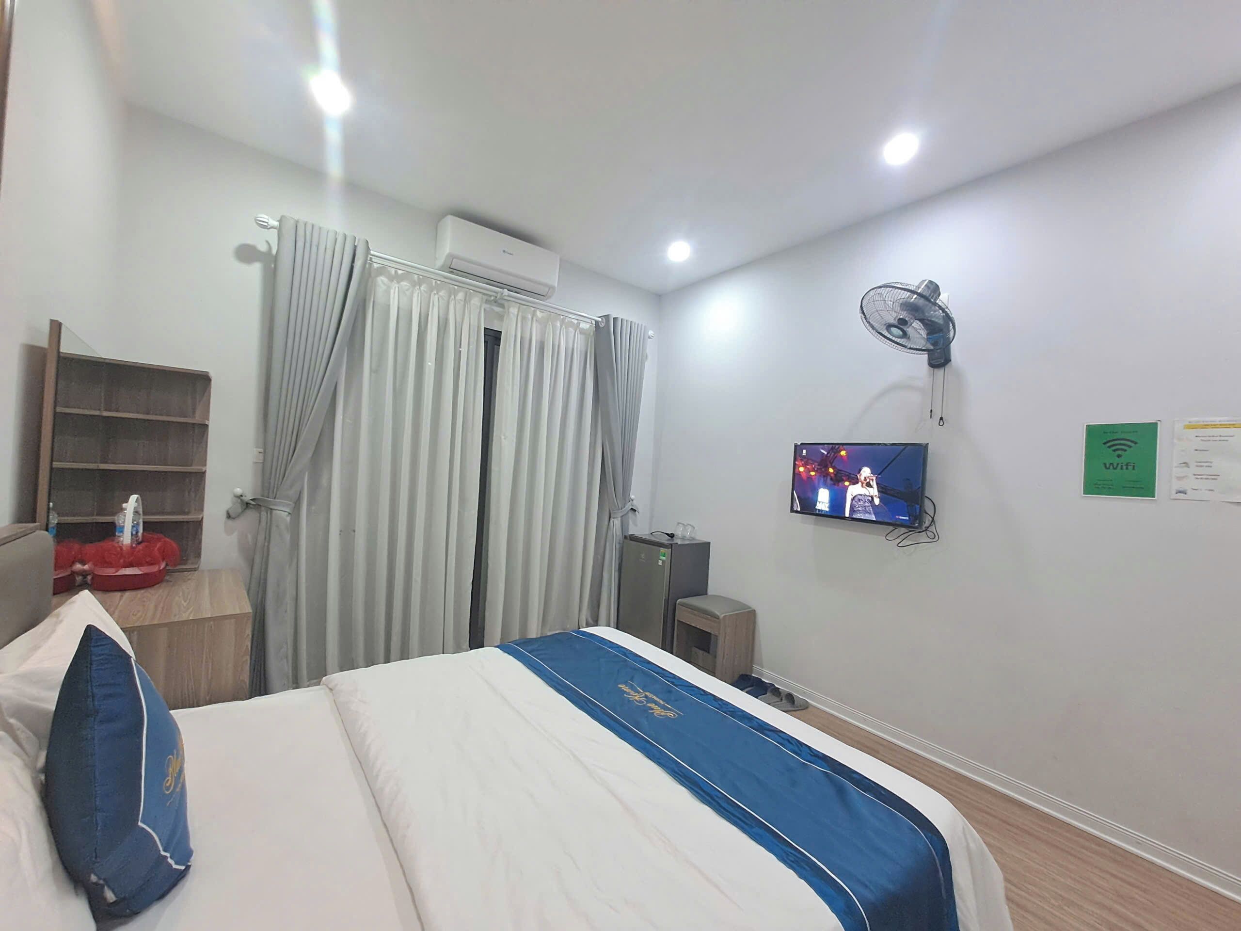 Une chambre d’hôtel équipée d’un lit, d’une télévision, d’un ventilateur et d’une étagère contenant des articles de toilette.