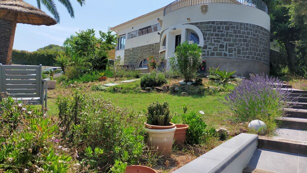 A house with a stone facade, a balcony, and a garden with various plants and a palm tree. - Logement de 50 m2 en rez de Jardin (Fréjus)