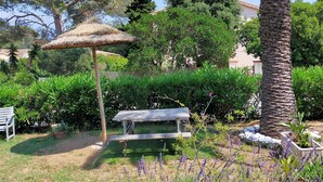 A garden with a thatched umbrella, a wooden bench, and a palm tree. - Logement de 50 m2 en rez de Jardin (Fréjus)