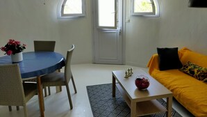 A room with a dining table, chairs, a sofa, a coffee table, and a door with windows. - Logement de 50 m2 en rez de Jardin (Fréjus)