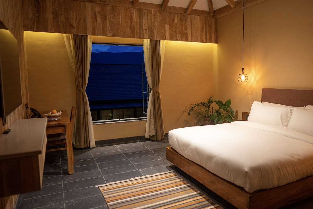 A bedroom with a bed, a desk, a window with curtains, a potted plant, and a night light.