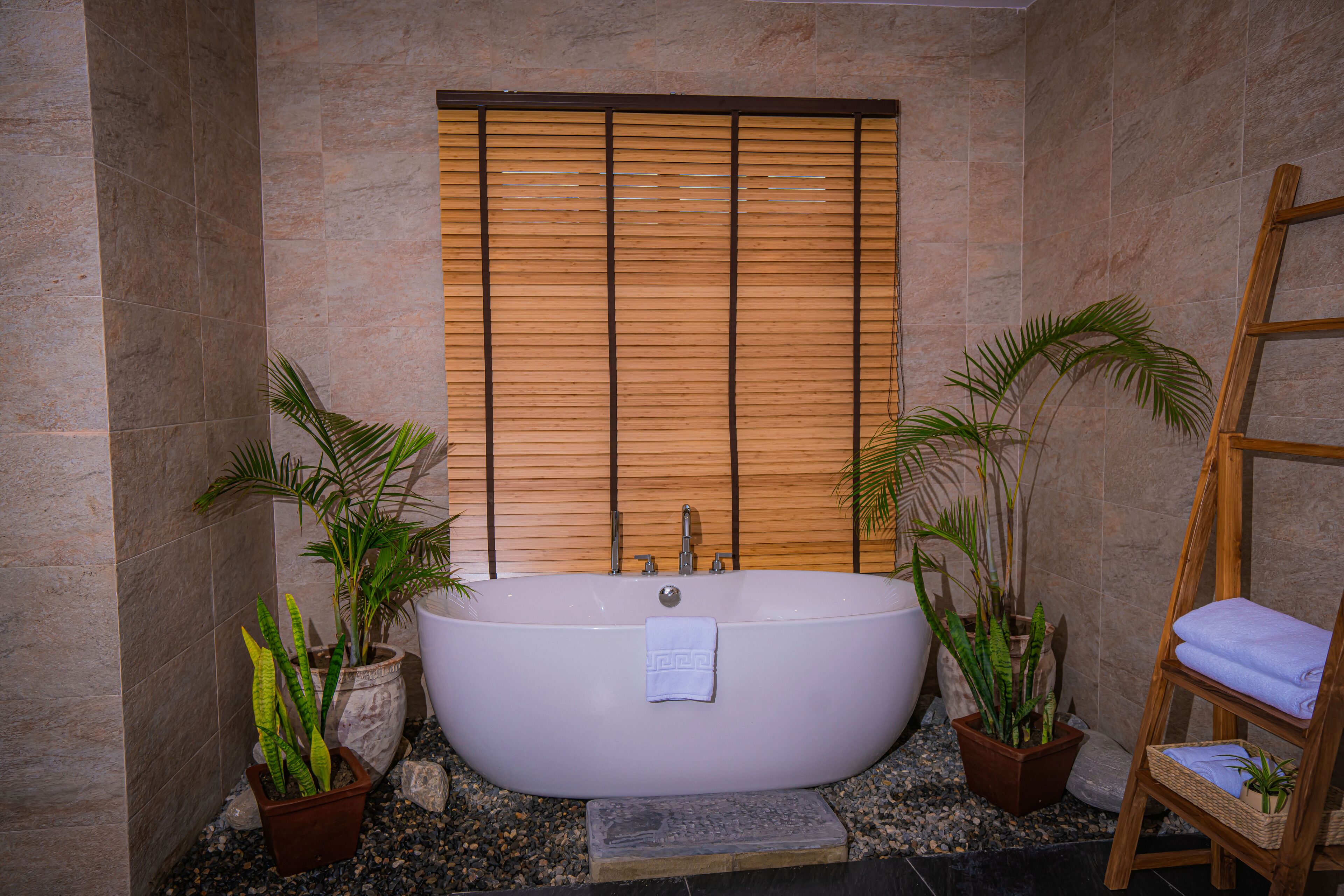 A bathroom with a freestanding bathtub, wooden blinds, and potted plants.