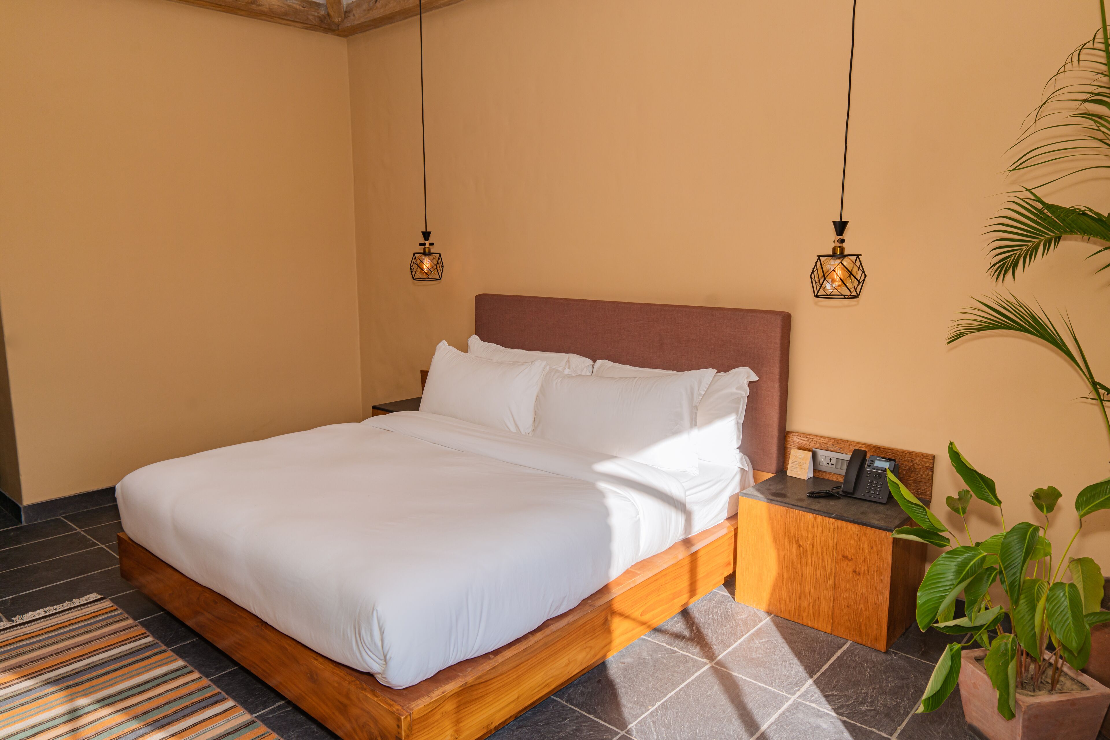 A neatly made bed with white linens, a wooden headboard, and a nightstand with a telephone and a small table.