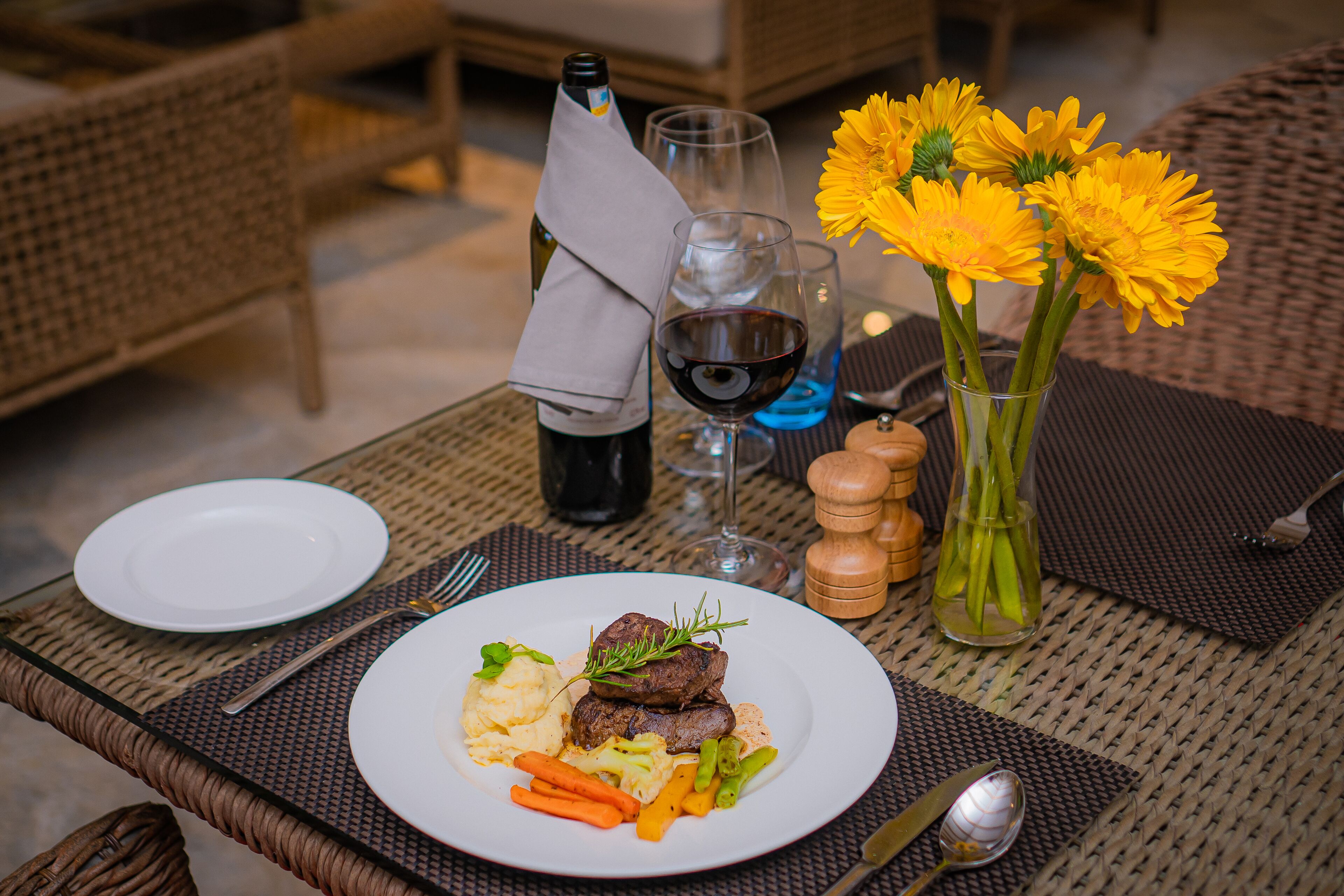 A dining table with a plate of food, wine glasses, a bottle of wine, and a vase with flowers.