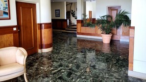 A lobby with a marble floor, wooden reception desk, and a staircase in the background.