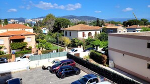 A residential area with parked cars, houses with red-tiled roofs, and a clear blue sky.