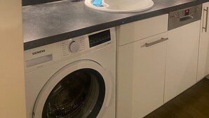 A modern kitchen with a built-in washing machine, a sink with a soap dispenser, and a glass cabinet above the sink.