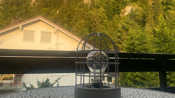 A balcony with a patterned tablecloth, a decorative light fixture, and a view of a mountain with a building in the background.