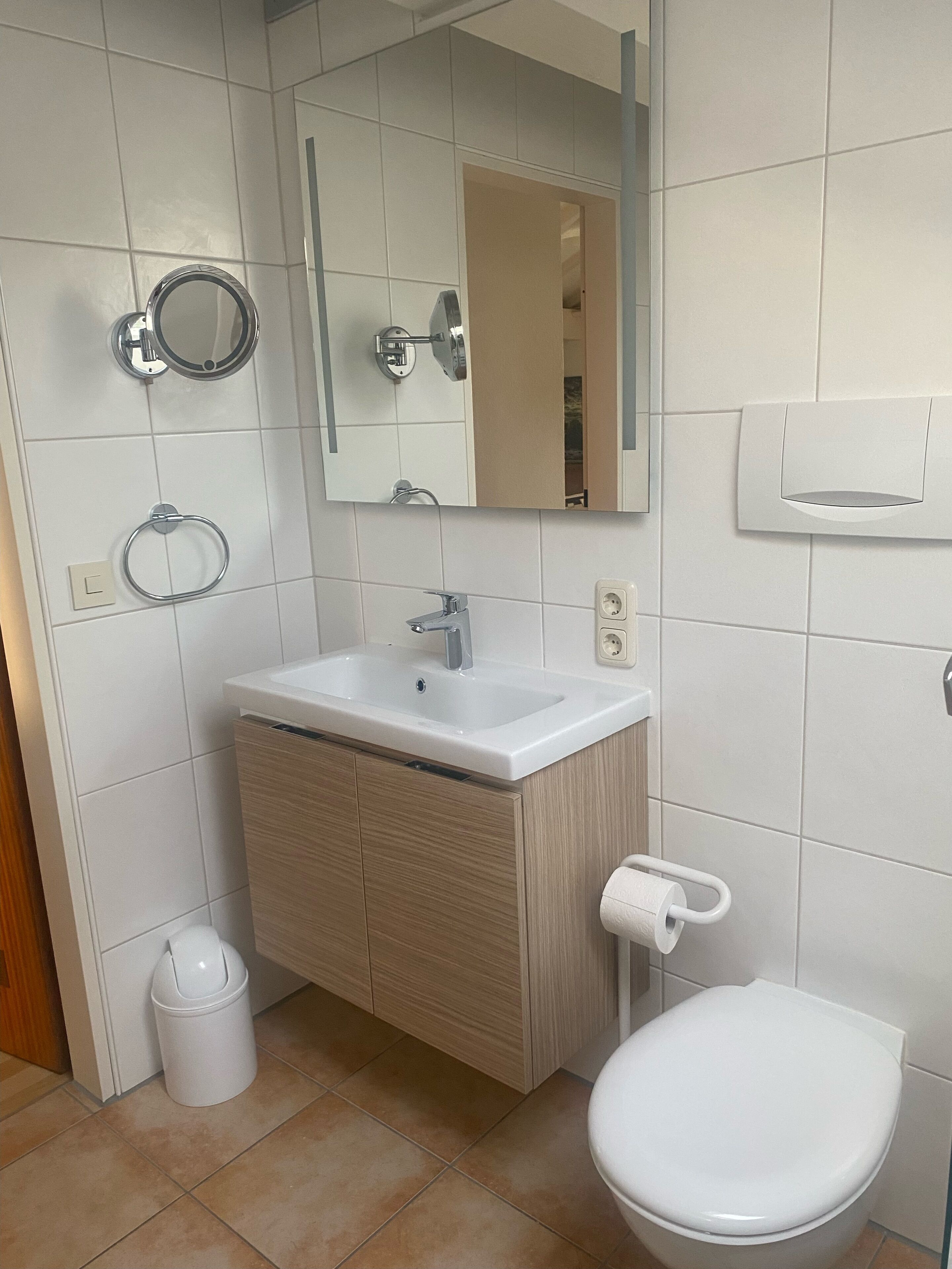 A modern bathroom with a white sink, mirror, and toilet.
