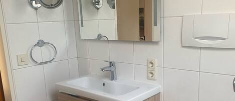A modern bathroom with a white sink, mirror, and toilet.