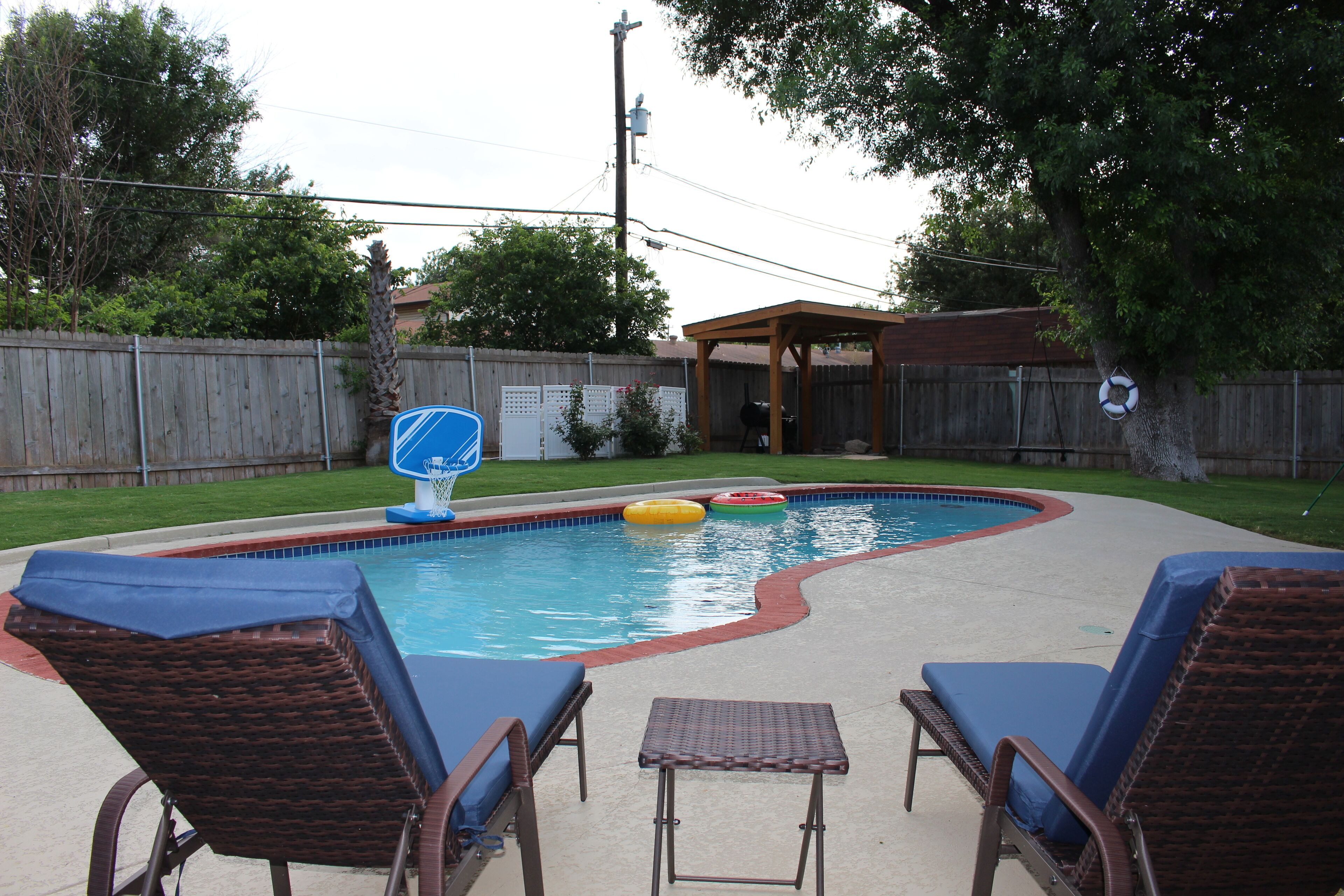 A backyard with a swimming pool, lounge chairs, and a small table.