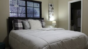 Una cama bien hecha con edredón blanco, cabecero y mesita de noche con lámpara.