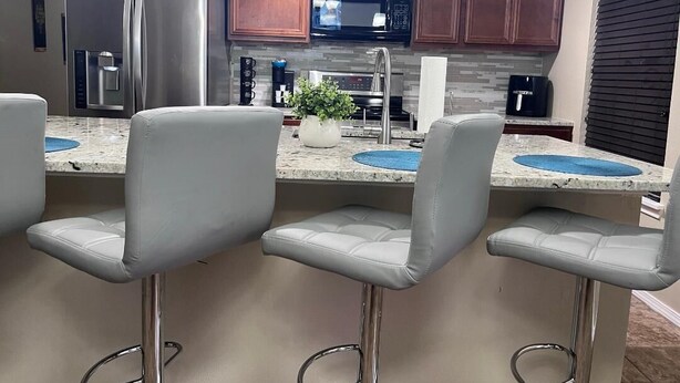 Una cocina moderna con electrodomésticos de acero inoxidable, encimera de granito y taburetes de bar.