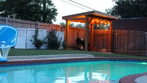 Un patio trasero con piscina, zona de barbacoa y aro de baloncesto.