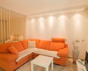 A modern living room with an orange sectional sofa, a white coffee table, and a decorative vase.