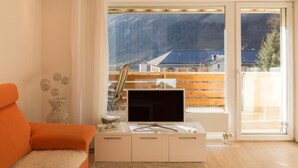 A modern living room with a large window, a flat-screen TV, and a sofa. - Haus Cristal  (Leukerbad)
