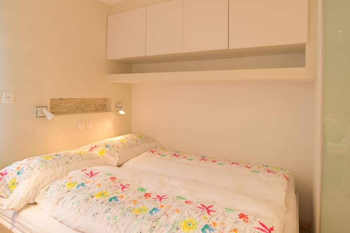 A bedroom with a bed, a wall-mounted shelf, and a wall-mounted light fixture.