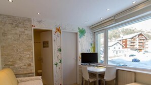 A room with a stone wall, a desk with a computer, a chair, a sofa, and a window with a view of buildings and snow. - Haus Cristal  (Leukerbad)