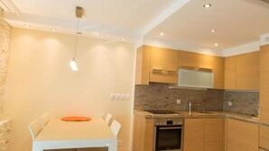 A modern kitchen with wooden cabinets, a built-in oven, and a dining area with a white table and chairs. - Haus Cristal  (Leukerbad)