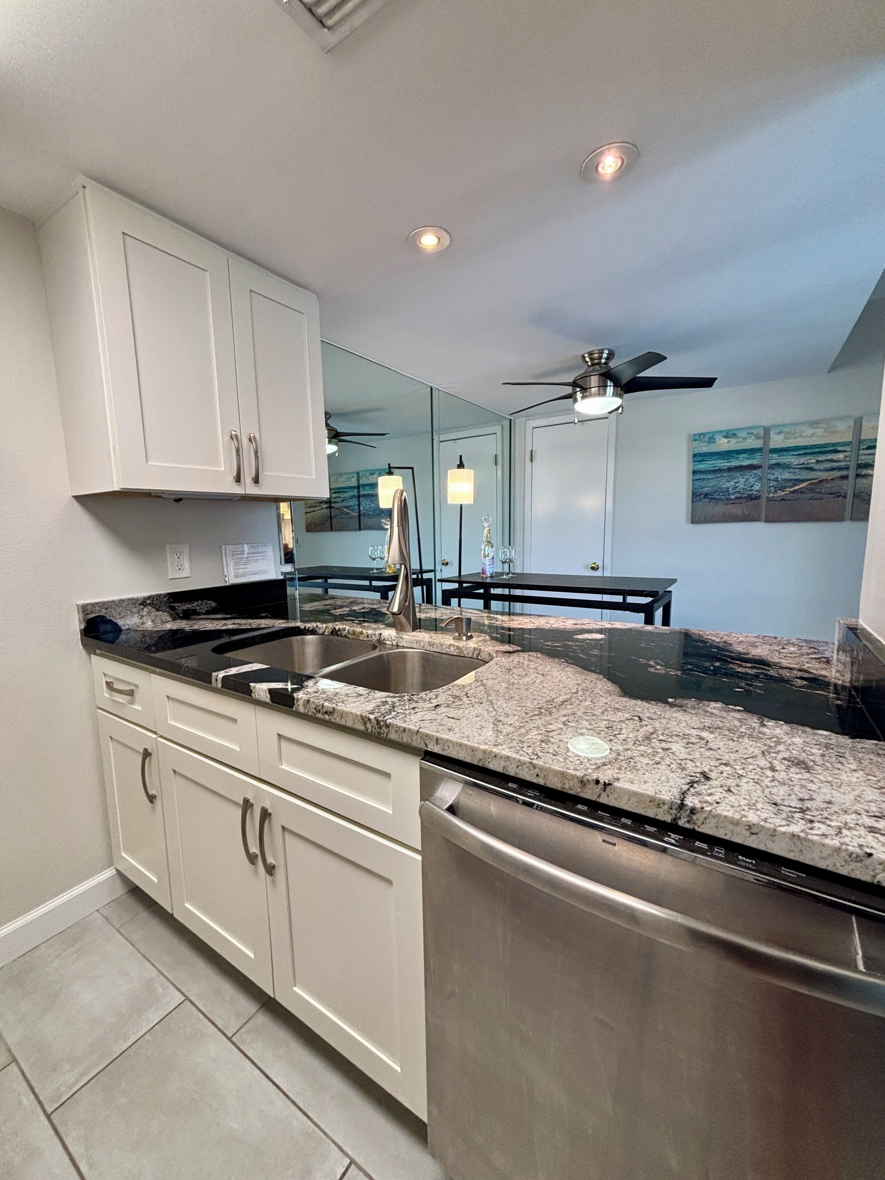 A kitchen with white cabinets, a stainless steel dishwasher, a granite countertop, and a ceiling fan.