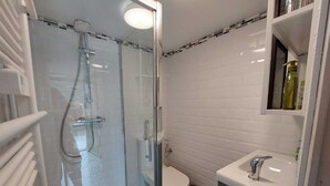 Un baño moderno con ducha de vidrio, paredes de azulejos blancos, inodoro y lavamanos con espejo.
