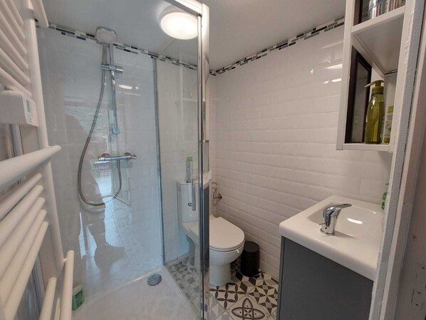 A modern bathroom with a glass-enclosed shower, white tiled walls, a toilet, and a sink with a mirror above it.