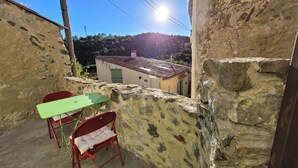 Un pequeño patio al aire libre con una mesa y sillas, un muro de piedra y vistas a un edificio con techo de tejas.