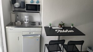 A compact kitchenette with a microwave, coffee maker, and sink. There is a small refrigerator, a table with chairs, and potted plants. - studio at carolina (Carolina)