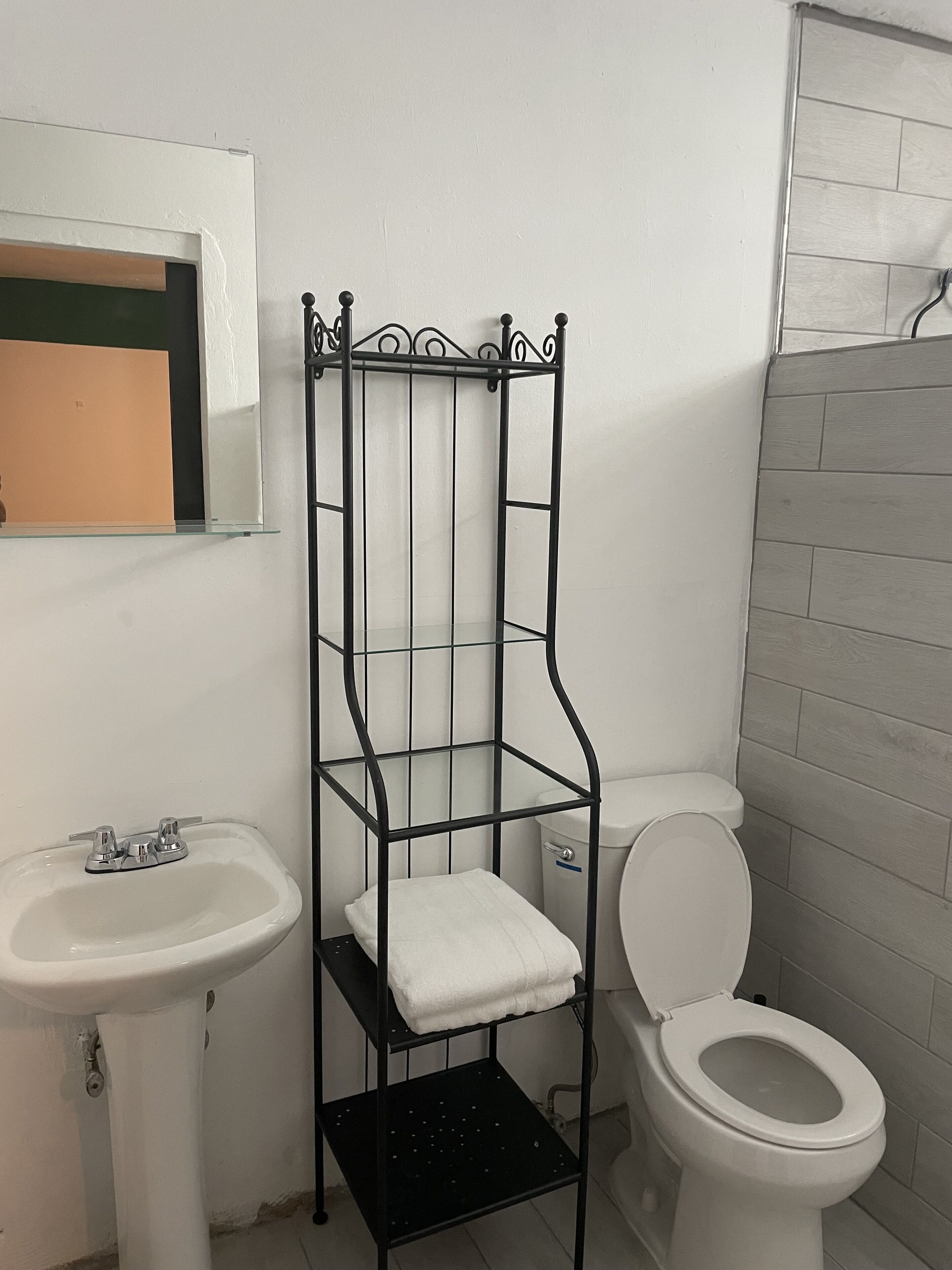 A bathroom with a white sink, a toilet, and a metal shelf with a white towel.