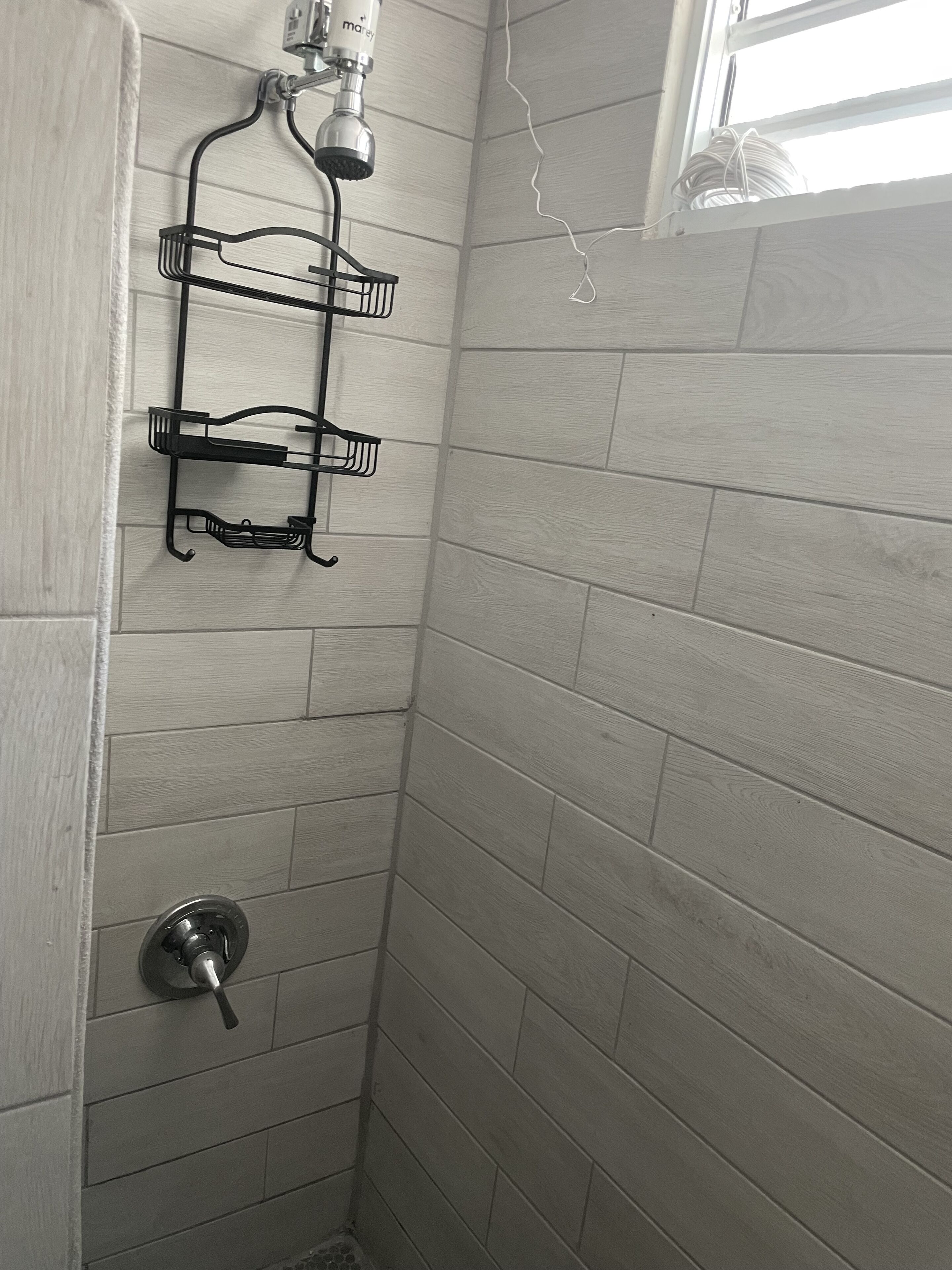 A shower area with a metal rack and a handheld showerhead mounted on the wall.