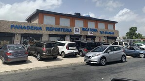 A building with multiple business signs including "PANADERIA," "REPOSTERIA," and "RICA DONA." Several cars are parked in front. - studio at carolina (Carolina)
