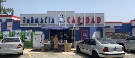 A pharmacy named 'Farmacia Caridad' with a blue and white facade, a storefront, and a parking lot with cars.