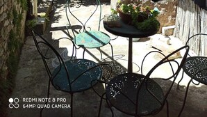 Un patio con paredes de piedra, una mesa con un cuenco y sillas de metal.