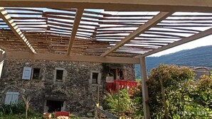 Un edificio de piedra con varias ventanas, una silla roja y una estructura de pérgola de madera.